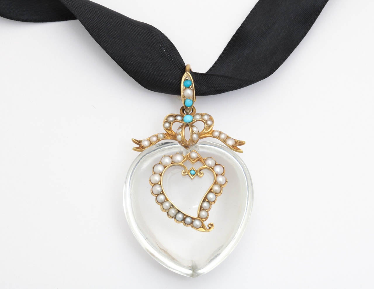 A fulsome rock crystal, clear and pure, holds a witch's heart of natural pearls. At its center sits a dot of turquoise that hypnotically holds the eye. The bale forms a flowing gold bow with its ribbons sitting atop the crystal like a crown. This