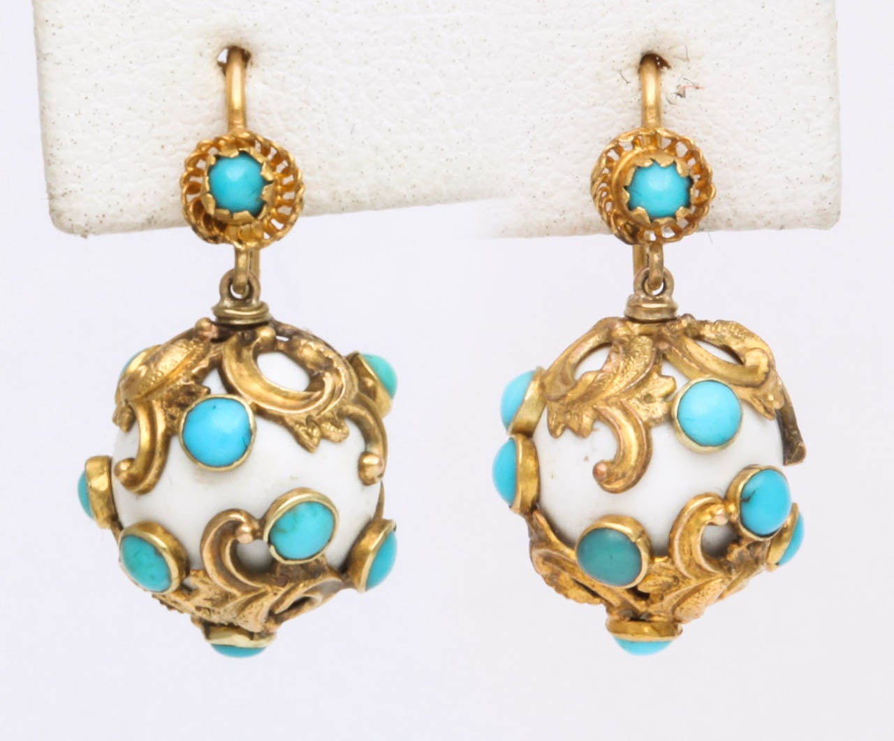 Fun and easily wearable, this pair of Victorian earrings is made with dangling orbs of white enamel wrapped in golden vines. The vines terminate in turquoise floral buds. At the earlobe is a  small flower also centered by a turquoise. Light in color