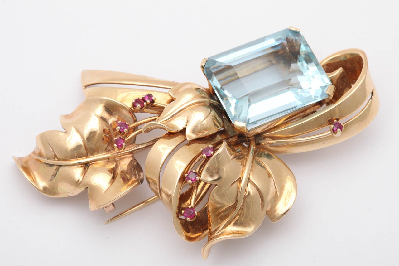 1940's Clip with a Faceted Aquamarine Embellished by a corsage of ribbons & leaves and sprigs of Rubies Set in 14kt Rose Gold. Ca. 1940. Aquamarine - approximately 25 cts.