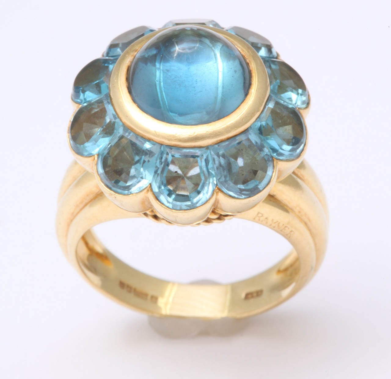 18Kt Yellow Gold ring set with Faceted Blue Topaz stones and a center Cabochon Blue Topaz  stone.  Signed Rayner on the outer shank and marked with British gold marks on the interior shank.