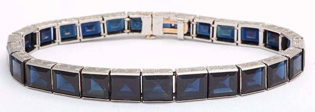 Art Deco straight line graduating sapphire bracelet containing 27 faceted square cut Australian sapphires channel set in a flexible box link platinum mounting.  The platinum bracelet is highlighted with scrolled hand etched accents on sides. The