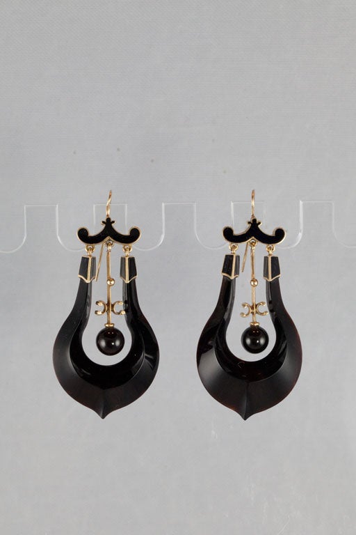 Each of these unique earrings is composed of a lyre-shaped semi-translucent plaque of black onyx, accented by 14 karat yellow gold and black enamel, suspended from the center an independently moving rod of gold with a bead of onyx. One of a kind!