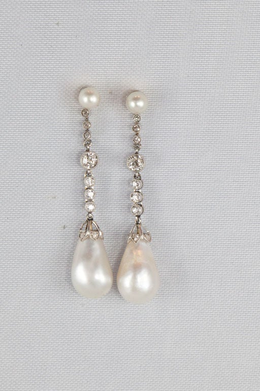 Each earring features 1 tear drop -shaped natural pearl in a pierced, saw-toothed platinum cap bead-set with rose-cut diamonds, suspended from a chain of 7 bezel-set old European-cut diamonds attached to 1 round natural pearl at the top. Pearls are