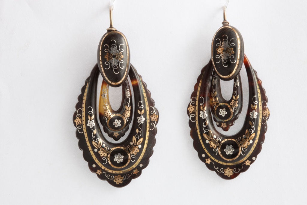Intricate and rambling flowers and vines are incised into natural tortoise shell which was shaped into elongated, scalloped hoops. The incised design was then inlayed with gold and silver.  This is a fine example of a lost art popular in France and