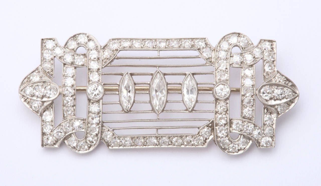 Like a musical notation, three marquise rest upon horizontal platinum bars. The surround is looped, and arched, encrusted with diamonds passing over and under ovals. There is a lot of geometry, all delicate, forming an elegant, sophisticated brooch