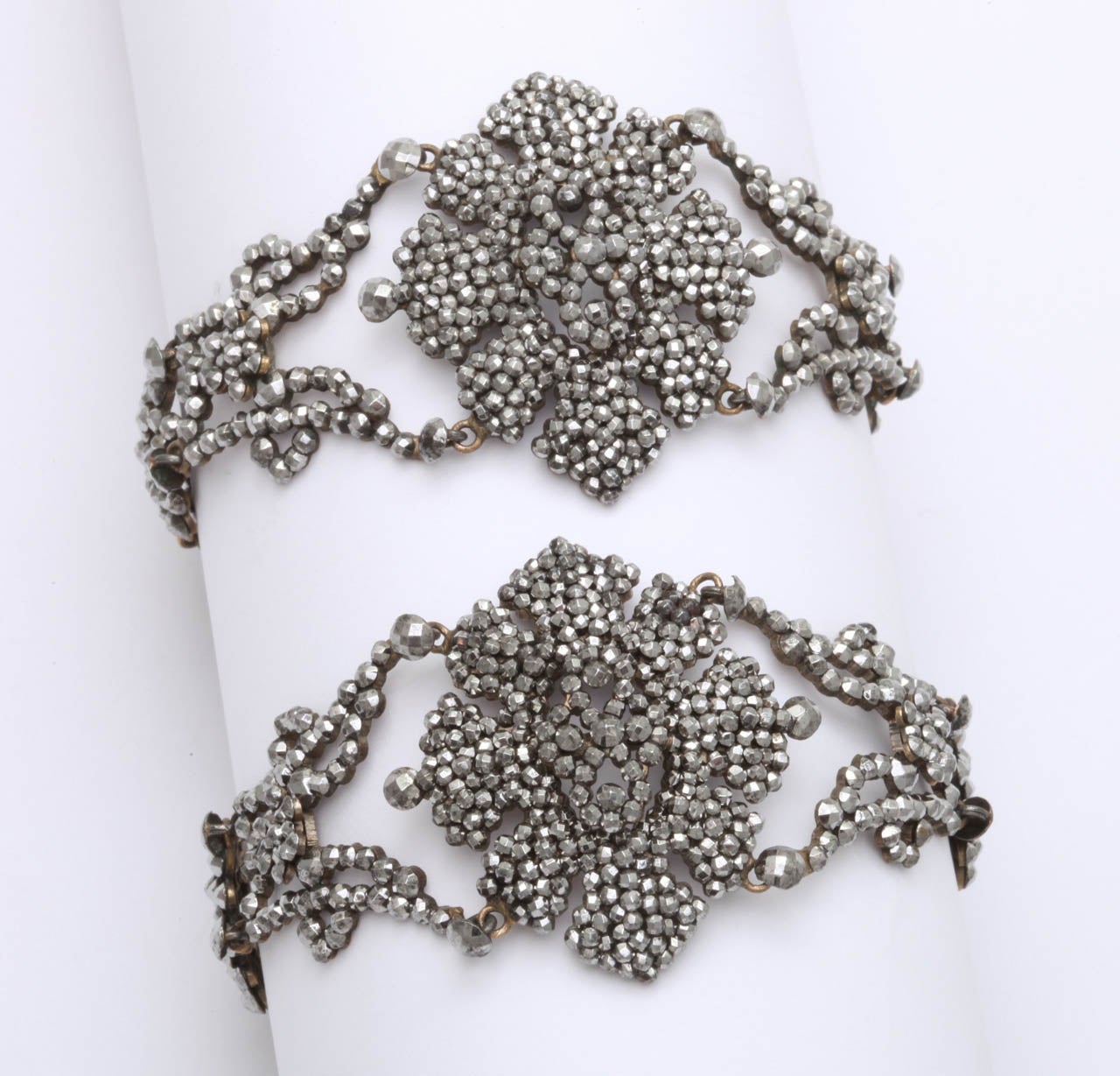 Two are better than one when you find a rare pair of cut steel bracelets made of tightly clustered cut steel rivets that form flowers and bows along the seven inch length these Georgian bracelets. The rivets are so small that they could be poppy