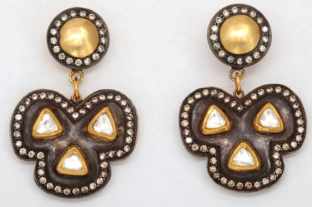 A pair of earrings composed of rhodium plated sterling silver, 18kt yellow gold and diamond clovers. The clovers are suspended from rhodium plated sterling silver and 18kt yellow gold studs, which have been set with diamonds. There are approximately