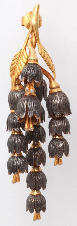 A pair of earrings composed of 18kt yellow gold leaves and rhodium plated sterling silver lily of the valley flowers which cascade down an 18kt yellow gold vine. Each flower has 18kt yellow gold pistons set with diamonds on the ends