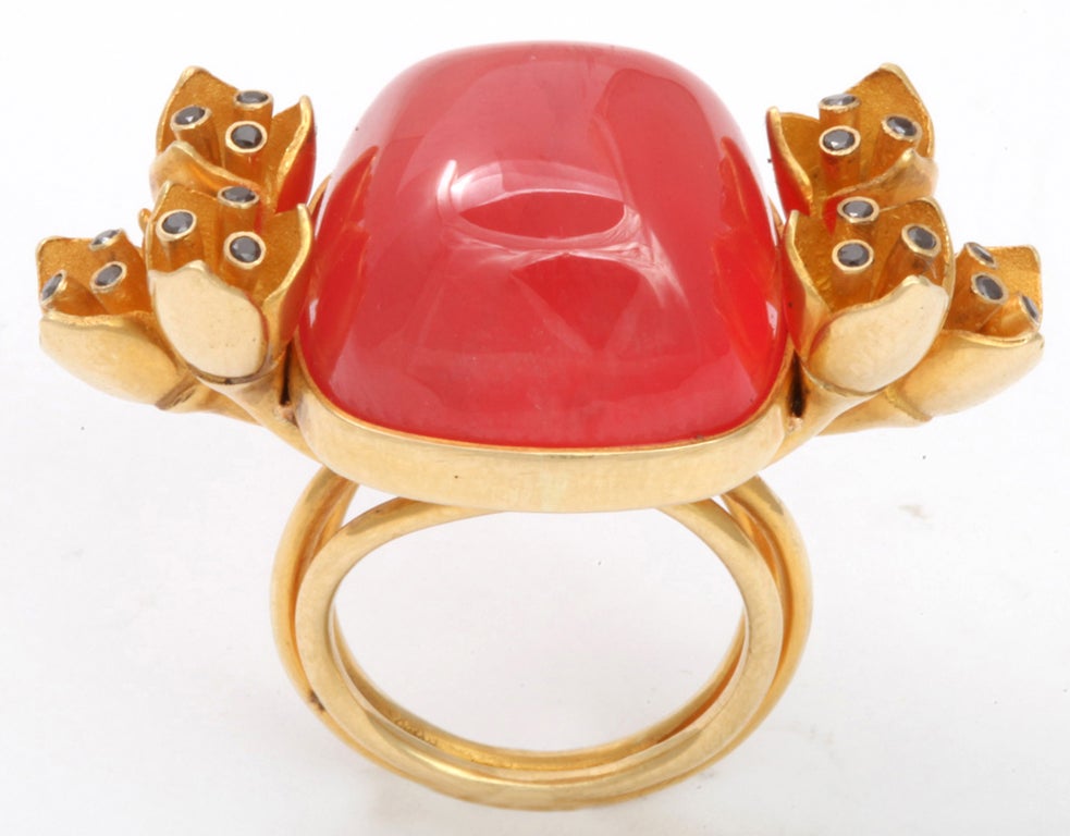 A ring composed of a rare sugarloaf rhodochrosite, weighing approximately 29cts,  set in an 18kt yellow gold bezel. The rhodochrosite is flanked on either side by three 18kt yellow gold tulips set with black diamonds in each pistil.
Size 7