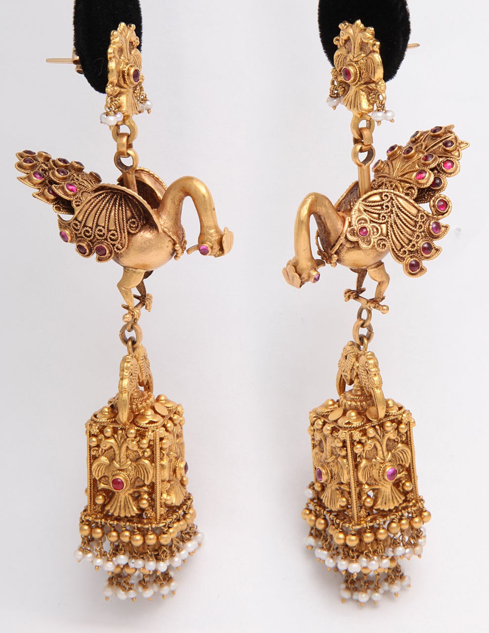A pair of earrings composed of 18kt yellow gold peacocks with bezel set cabochon ruby eyes and feathers. The peacocks suspend 18kt yellow gold  cages. The cages showcase four bird plaques. The cages have 18kt yellow gold and pearl fringe at the