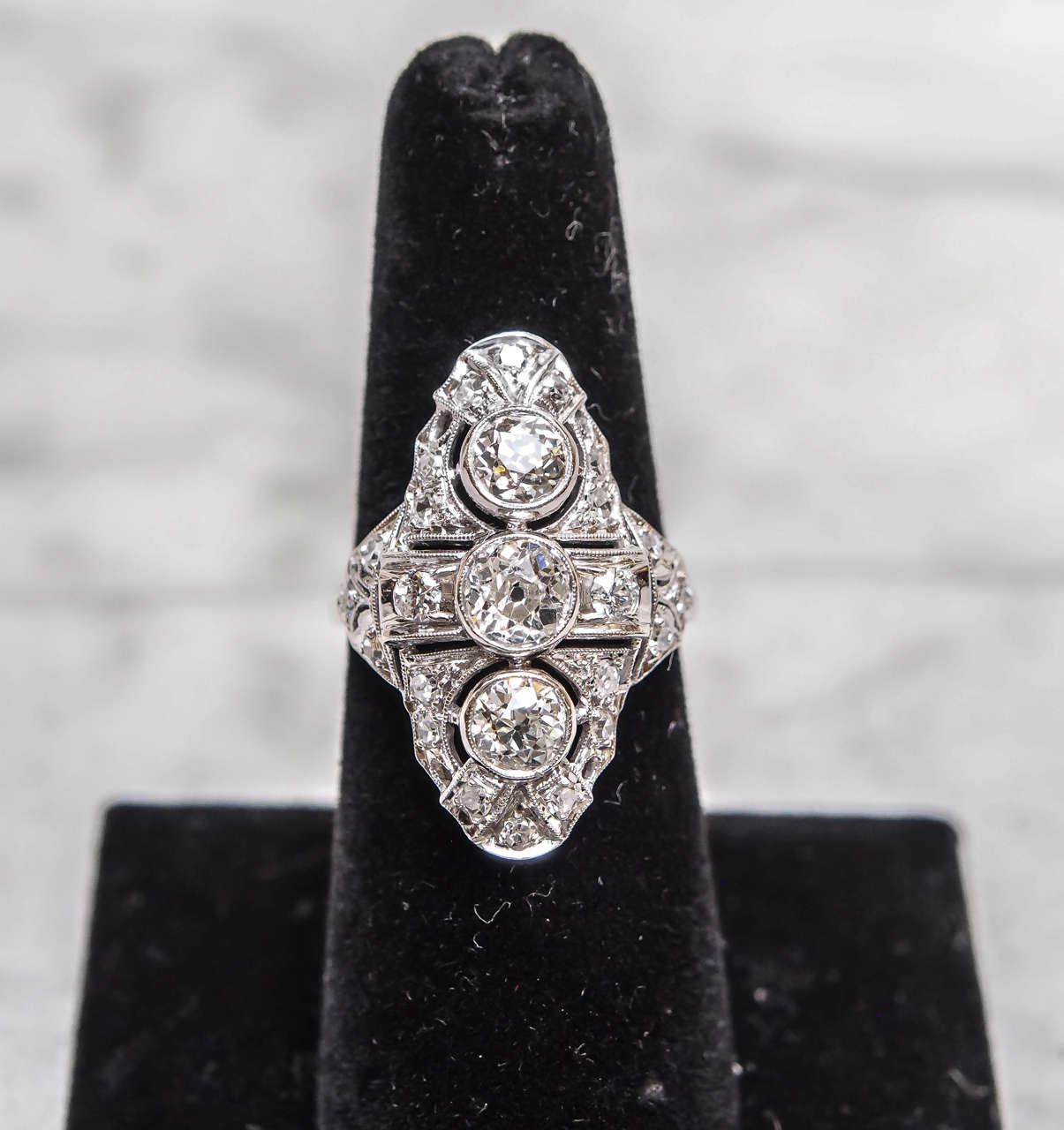 Period Art Deco Diamond Ring. The ring has three large diamonds down the center. The center diamond weighs approx. .75cts and the diamonds on either side weigh approx. .65cts each. The smaller diamonds around the ring weigh approx. .50cts. The total