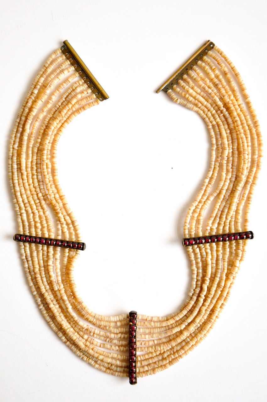 Elegant high-styled collar made of multi-strands of puka beads with garnet spacers.  Originally purchased at Stanley Korshak's in Chicago. Sits very comfortably on a small neck.
