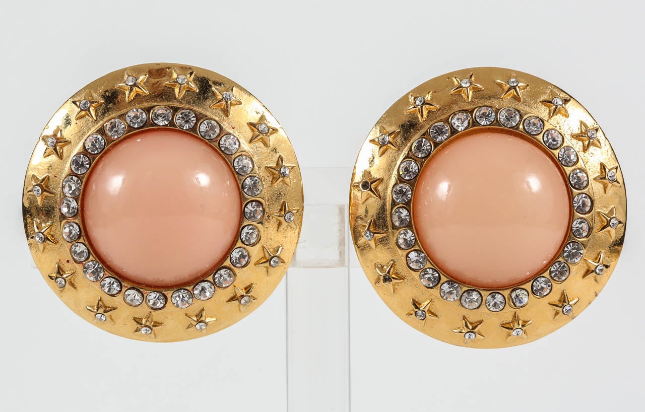 A chic pair of ear clips with a faux coral glass center surrounded by rhinestones and a frame of raised rhinestone-set stars. Marked on the back with just the Chanel name, indicating these are earlier Chanel, most likely from the late 50s/early 60s.