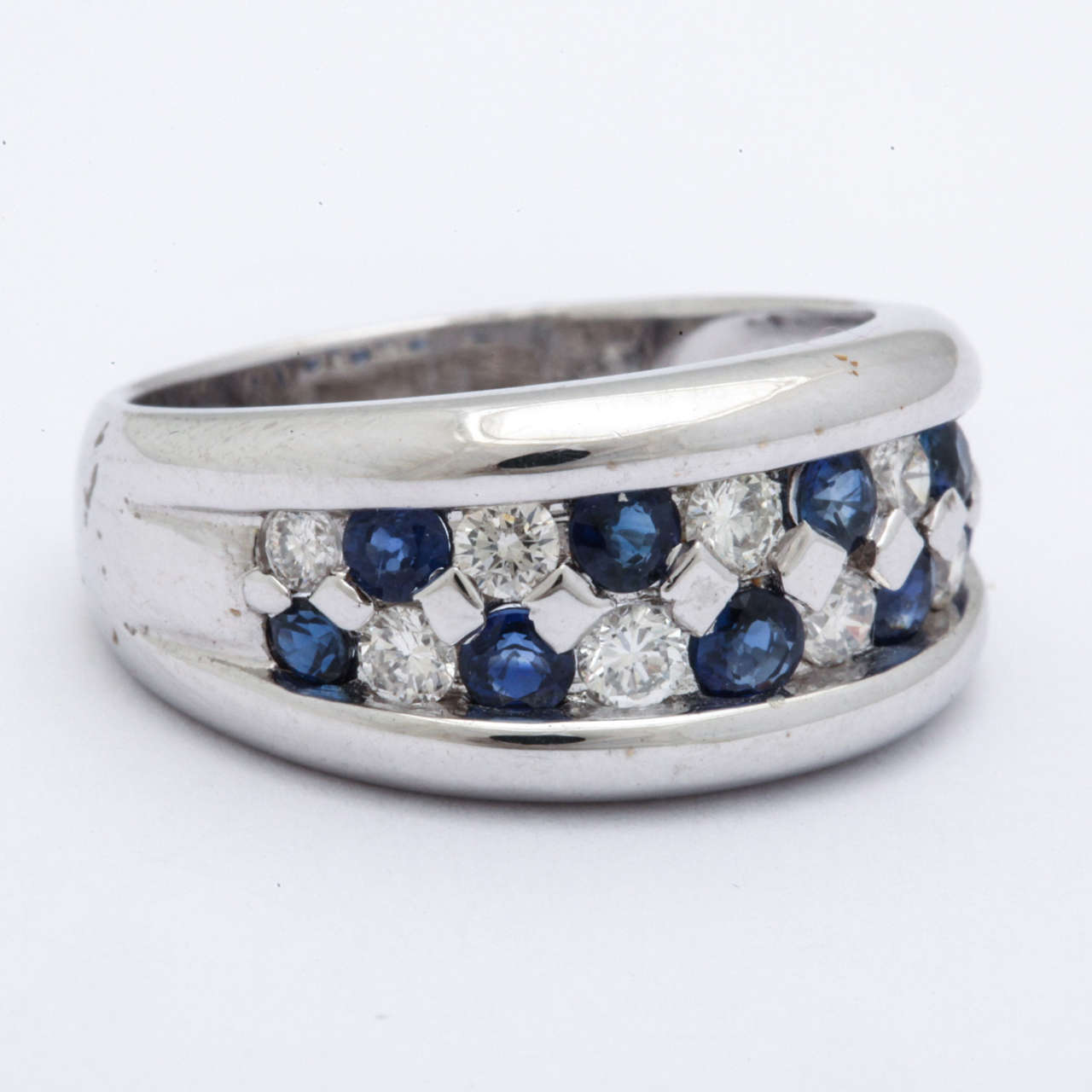 This 18 kt band ring has alternating blue sapphires, .62 cts and white diamonds, .48 cts. The rounded white gold bands on either side of the stone makes the ring bold and modern. It is a size 7.5 now and can be sized to your needs.