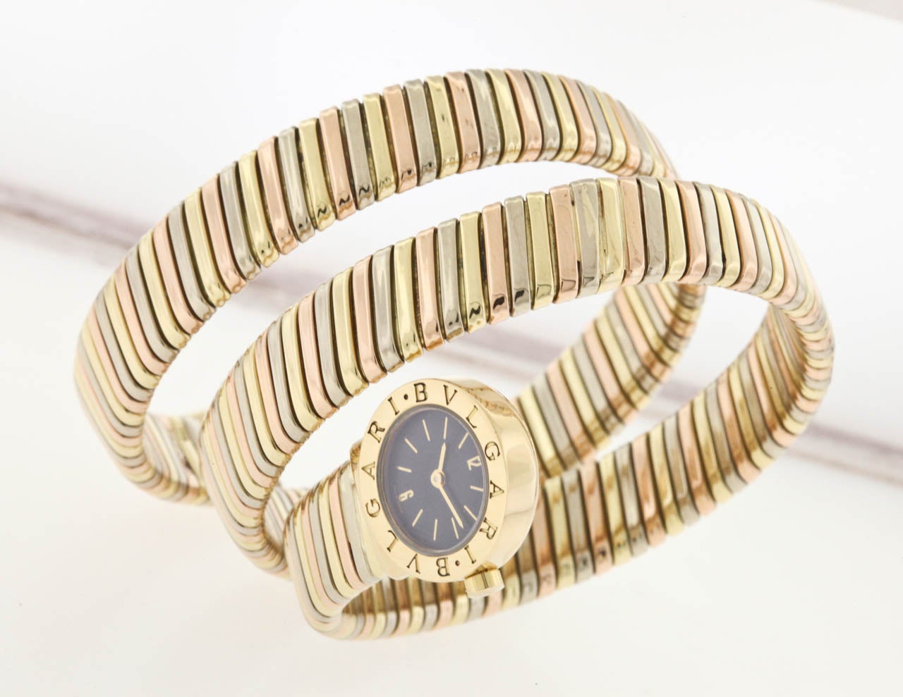 18k three-color rose, yellow and white gold Bulgari lady's Tubogas bracelet watch, circa 1990s. A wraparound gold bracelet with 19mm wristwatch case, snap back, quartz movement, black dial with applied hour indexes, Arabic 12 and 6, sapphire