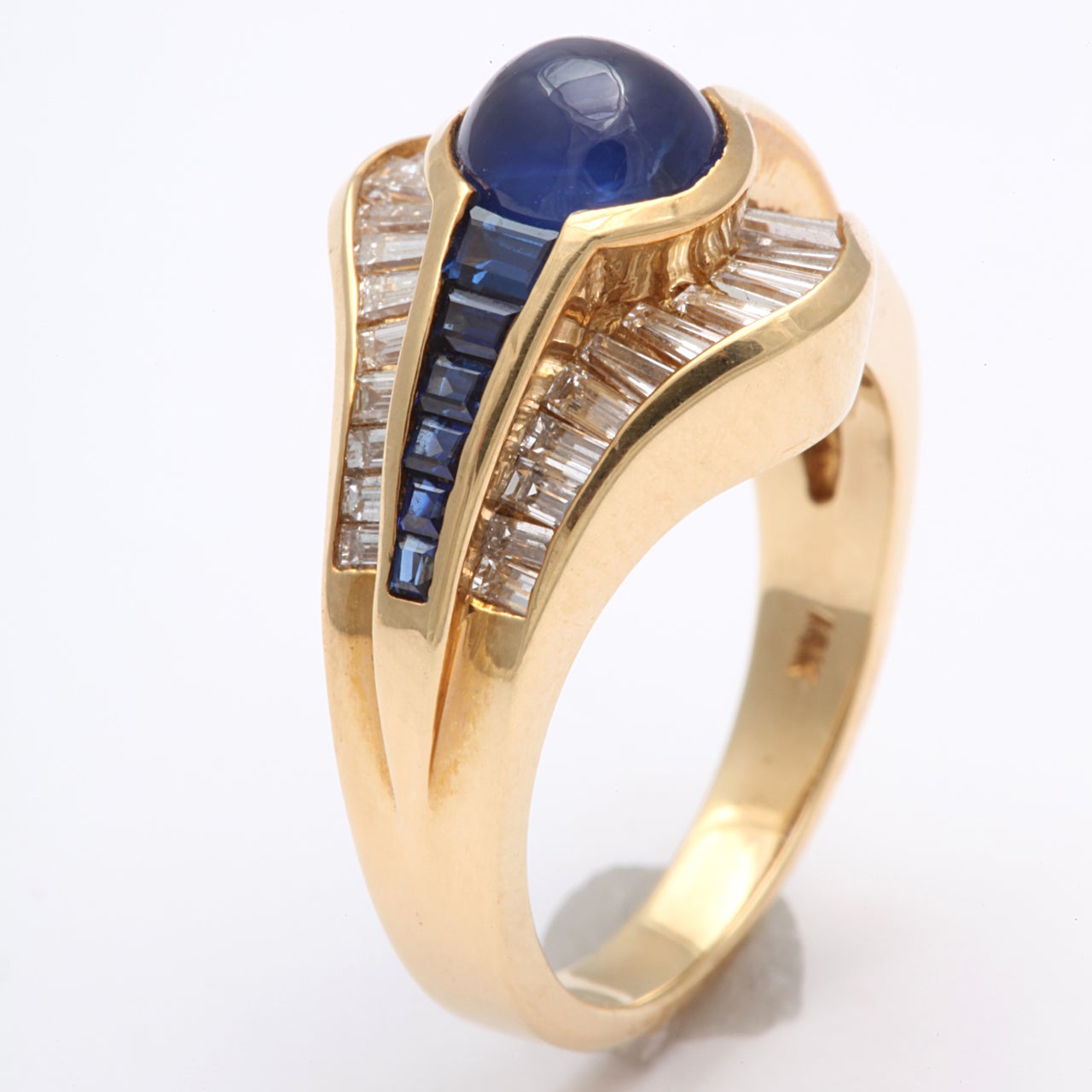 Super elegant Cabochon Sapphire Ring with tapered Channel set Sapphire Baguettes on either side and flanked by tapered Diamond Baguettes framing the Center Sapphire.  Set in 18kt Yellow Gold.