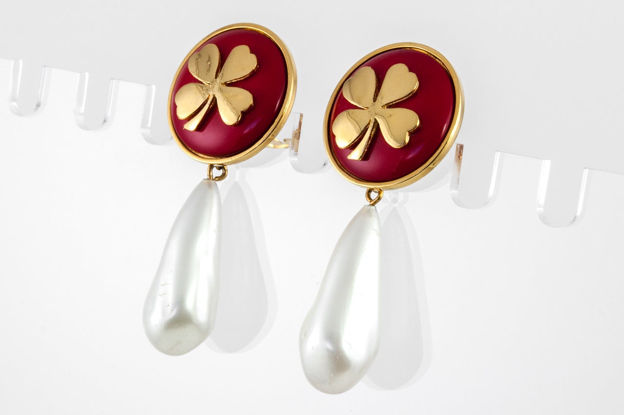 A pretty pair of ear clips by Chanel featuring a gilt metal clover set on red resin with a glass pearl teardrop dangling from it. Stamped on the back 