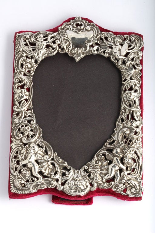 Sterling silver, heart-shaped picture frame, Dominick and Haff, New York, Ca. 1895. Sterling silver is pierced and decorated with cherubs, the North Wind, flowers, etc. Frame stands @8