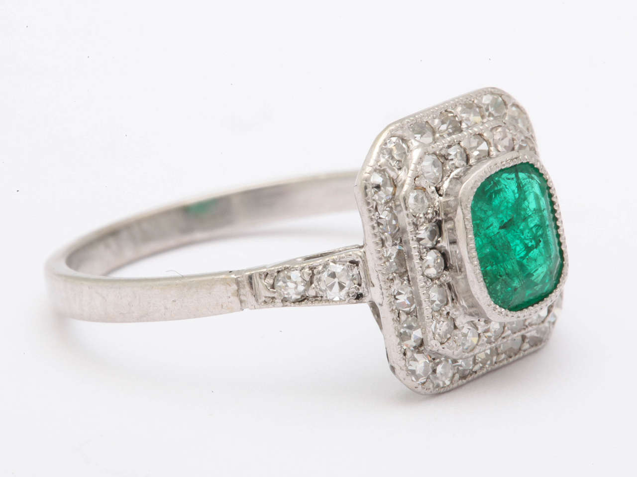 A lovely early 19 the century ring, constructed in platinum with 2 stepped tiers of pave set diamonds. The center stone is a classic bright green color and is approximately 5 by 6 mm  cushion cut natural emerald.