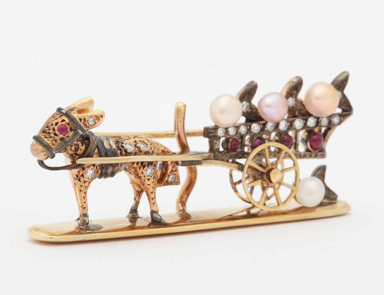 This lazy little donkey is pulling a cart loaded with diamonds and pearls.  The pin is made of 18 kt gold and silver, rubies, diamonds and pearls. There is a gooseneck hook at the back of the pin where a drop/pendant of pearls or stones  or anything
