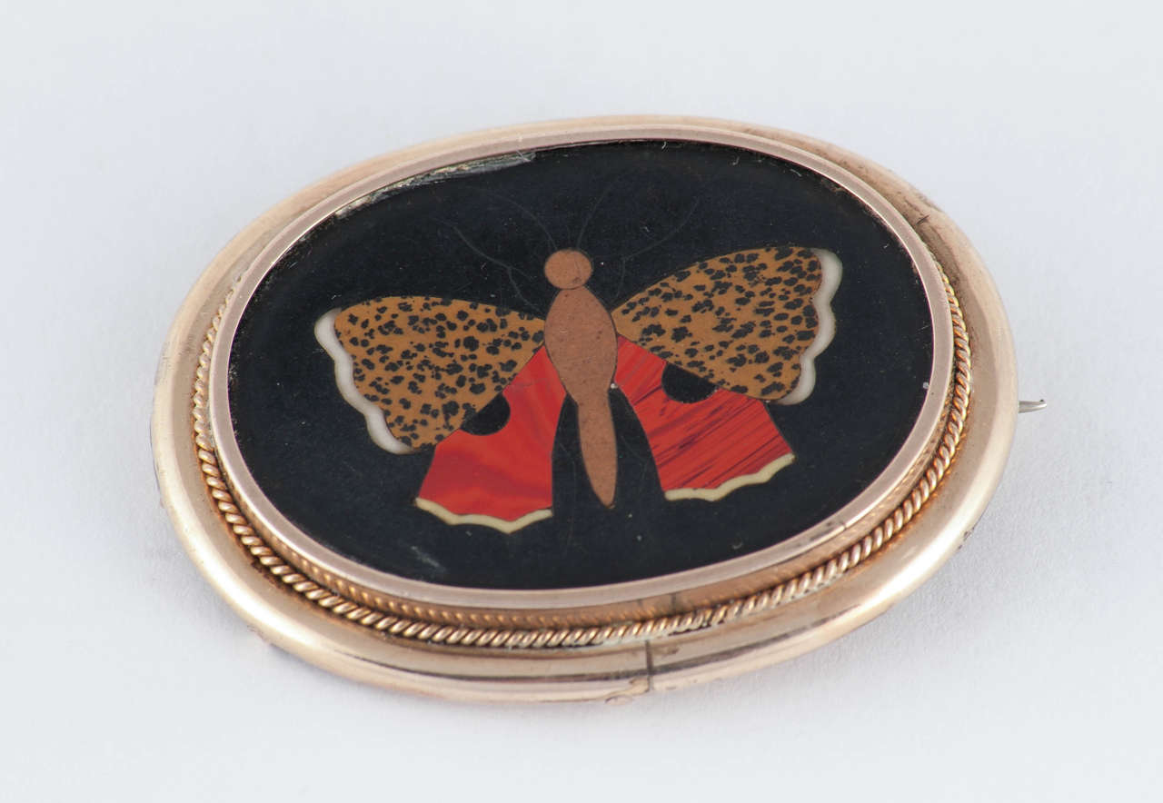 Lovely Victorian pietra dura pin of a butterfly in set in 9K gold. Pietra dura is a form of mosaic made with pieces of hard stone such as agate, as in this piece, cemented into black marble. It is also know as Florentine mosaic as Florence, Italy