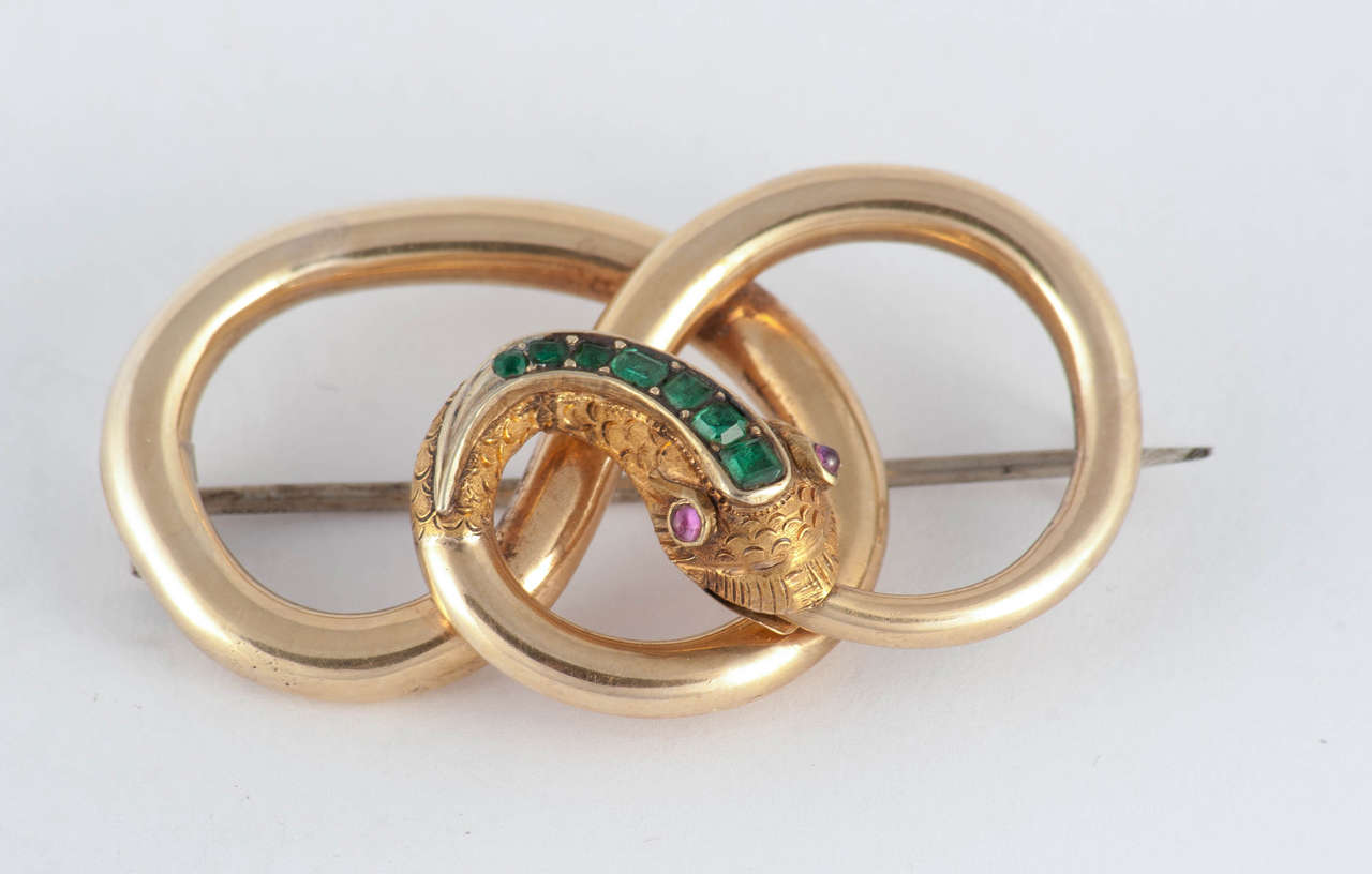 Victorian 18K gold swirly snake pin set with a row of emeralds along its head and ruby eyes. Snake jewelry became popular in the late 19th Century when Victoria received a snake ring as her engagement ring from Prince Albert. The snake holds his