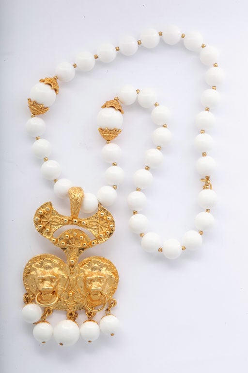 White beaded necklace spaced with tiny goldtone beads with a large goldtone double lion face pendant.