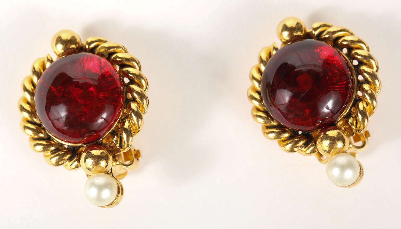 A lovely pair of Chanel ear clips with a cranberry poured glass center cabochon surrounded by a gilt metal rope detail and a glass pearl at the bottom. Marked on the back 