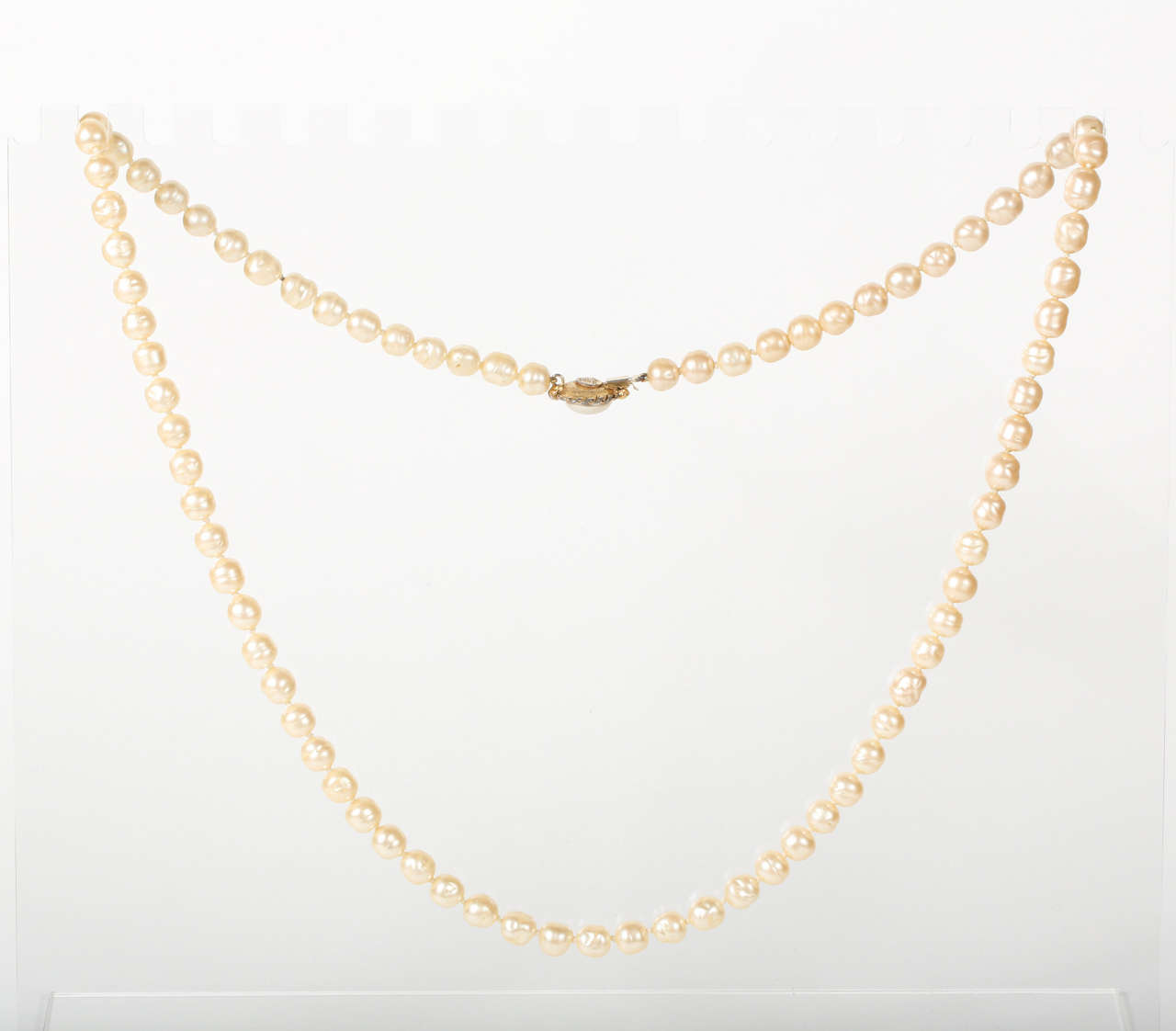 A beautiful glass pearl necklace with a large pearl button clasp surrounded by a gilt metal rope frame. This necklace is long enough that it could be doubled up. The back of the clasp features the 