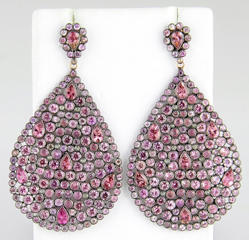 These earrings resemble a stained glass window. These teardrop earrrings contain bezel set pink sapphires with diamond highlights. The teardrops / pear shaped drops dangle off of an pink sapphire teardrop stud. The sapphires are set in sterling