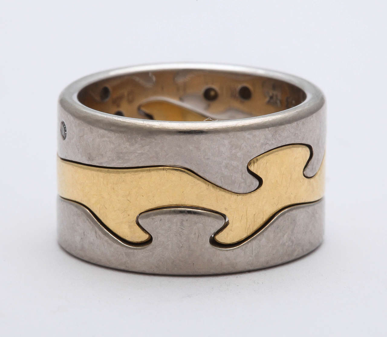 Fusion Ring by Nina Koppel.  Three interlocking bands - in this case - two outer 18kt White Gold bands set with abstract and randomly placed Diamonds centering on an interlocking 18kt Yellow Gold Band.  Marked Denmark & 53.
Quite magical as they