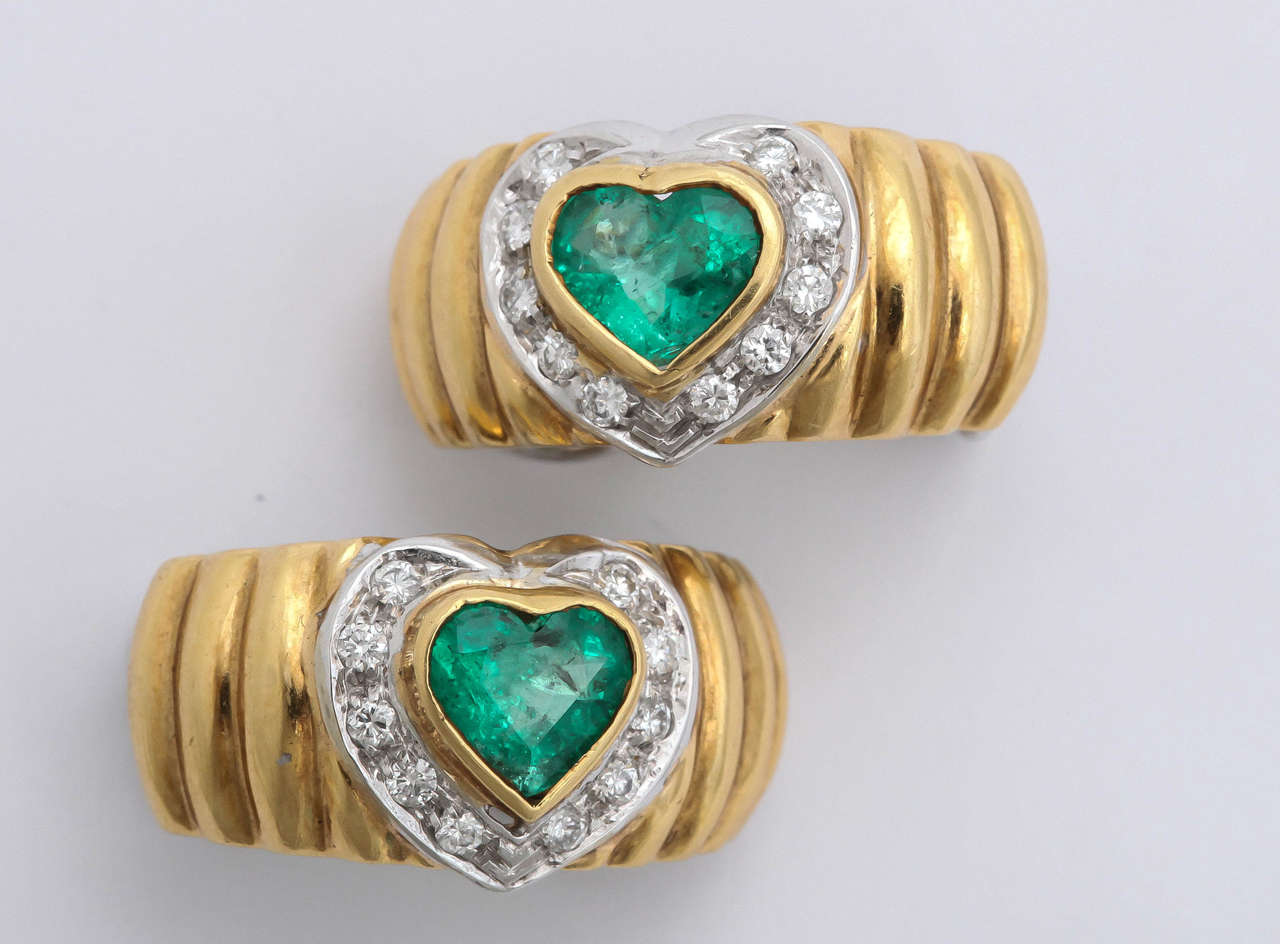 Chic pair of 18kt Yellow Gold Ridged Hoop Earrings each set with faceted Emerald Hearts surrounded by 10 clean white full cut Diamond set in white Gold. Made in Italy.