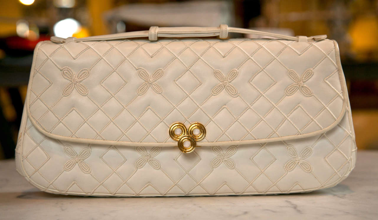 never used judith leiber clutch featuring opulent quilted surround with lovely embroidered floral accents. stunning geometric brass closure. ready to wear as clutch, handbag, or crossbody.(optional leather strap). debuts in pouch with original