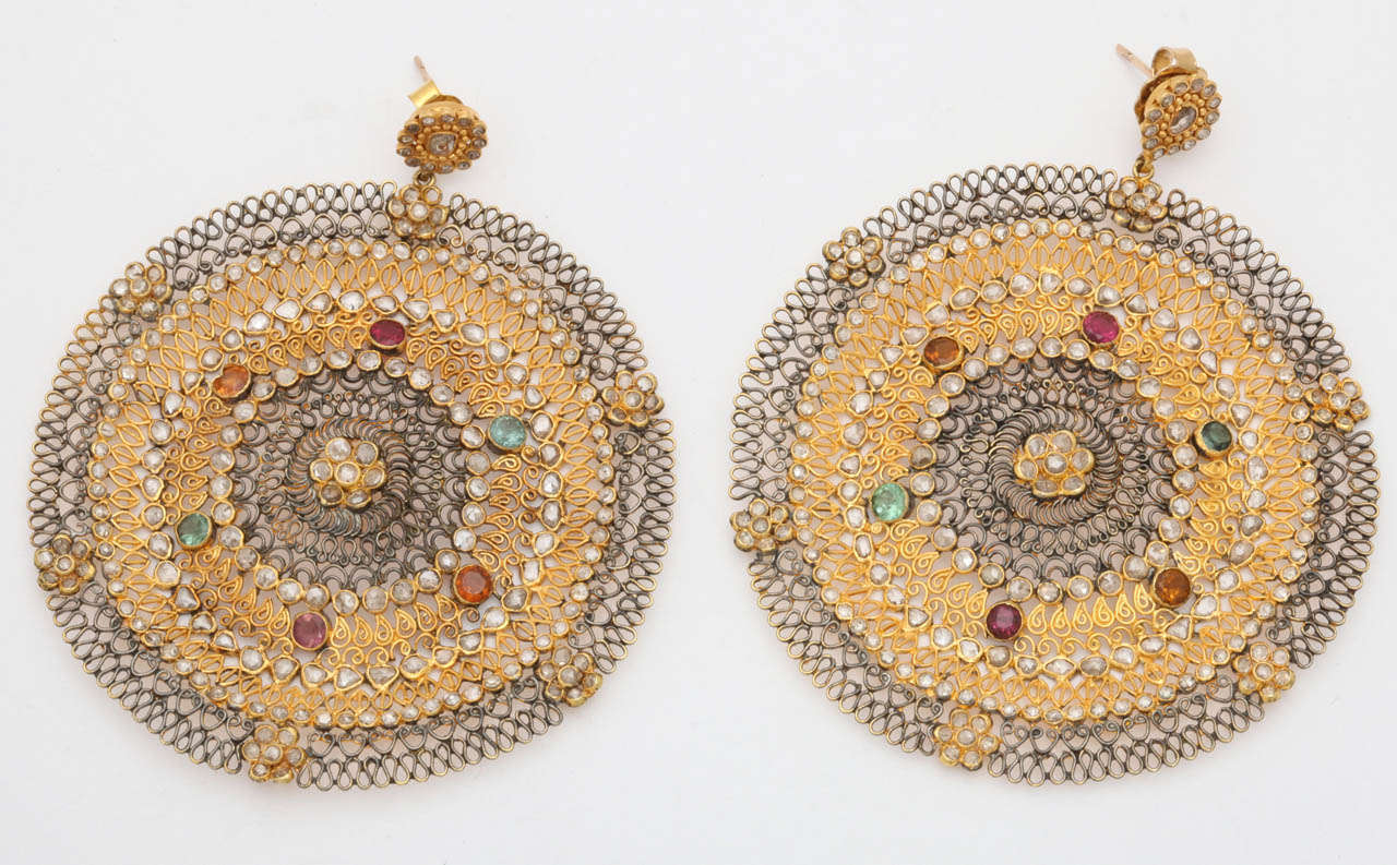 A pair of 18kt yellow gold hand woven earrings. The earrings  inner circle and outer rim have been rhodium plated. There are three rings of bezel set rose cut diamonds and there are rose cut diamond flower clusters around the border of the earrings.