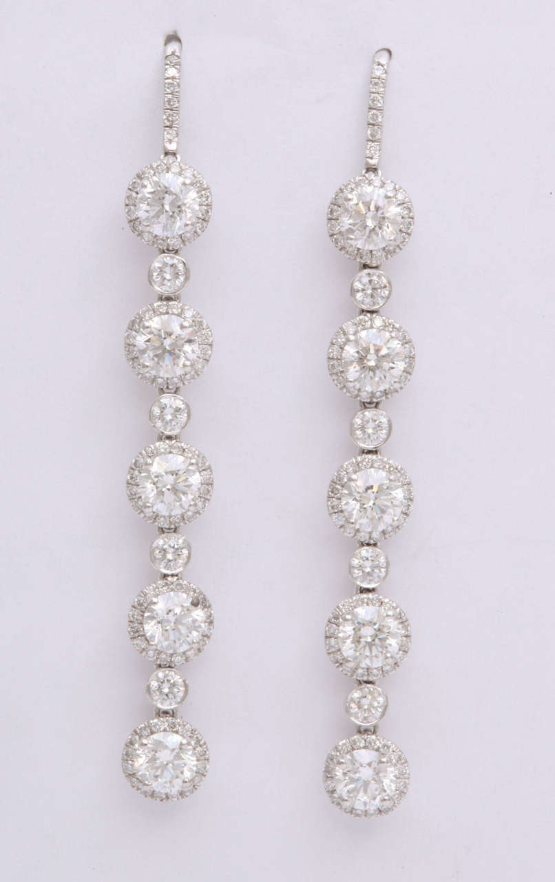Gorgeous platinum drop earrings featuring 10 round cut diamonds, each with a pave diamond halo. Total Weight: 4.08 carats.