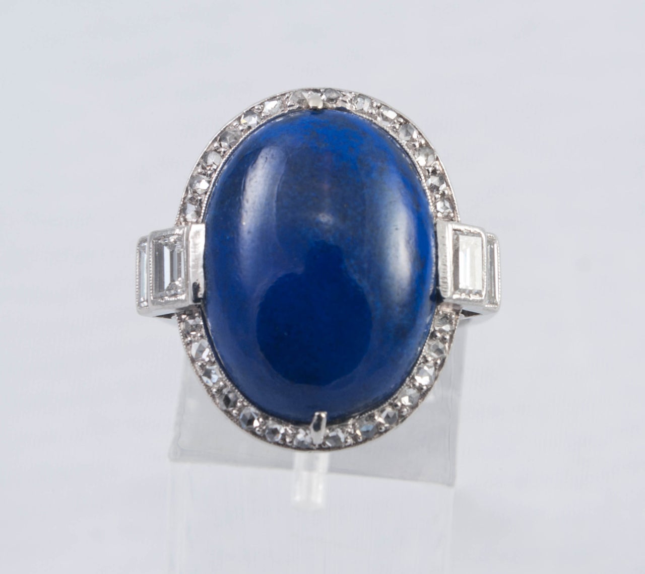 Cabouchon cut Lapis Lazuli ring surrounded by mixed cut small Diamonds and Baguettes set in Platinum ( tested ). It is engraved under the bezel with a fine reeded shank