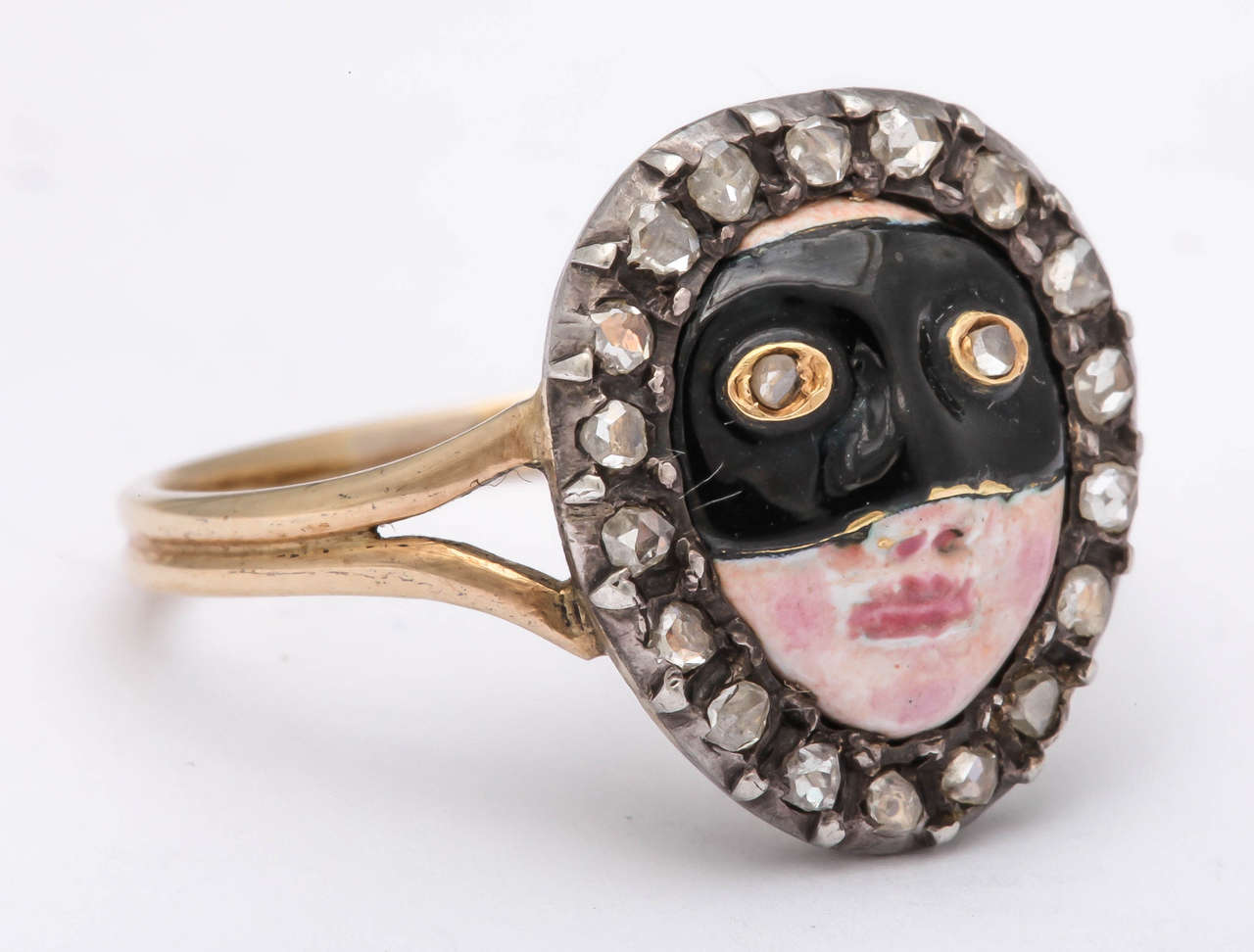 A lady’s face in enamel, with rosy cheeks and painted lips, wearing a black domino with rose diamond eyes, the border set with rose diamonds mounted in silver and gold. The reverse is designed as a gold shell.

Size 7 1/4.

France, 18th