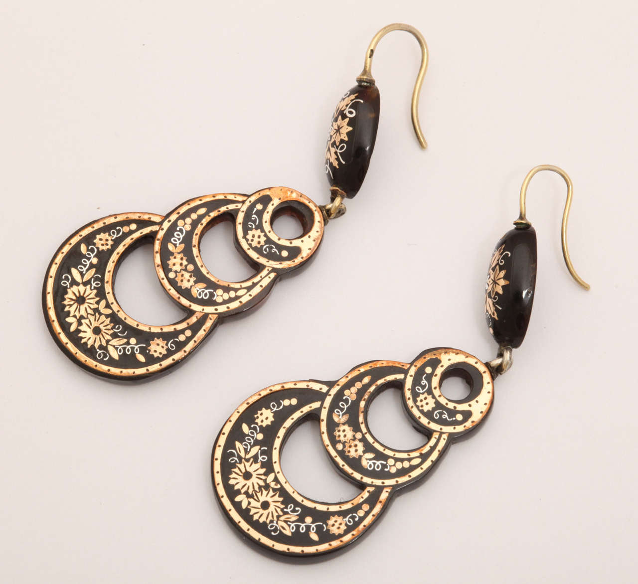 Floral wreaths of gold accented with silver fill the rings of these luscious pique earrings. An oval of the same floral display is attached to the wire. We found these earrings in original condition with ear wires intact. The rings are connected.