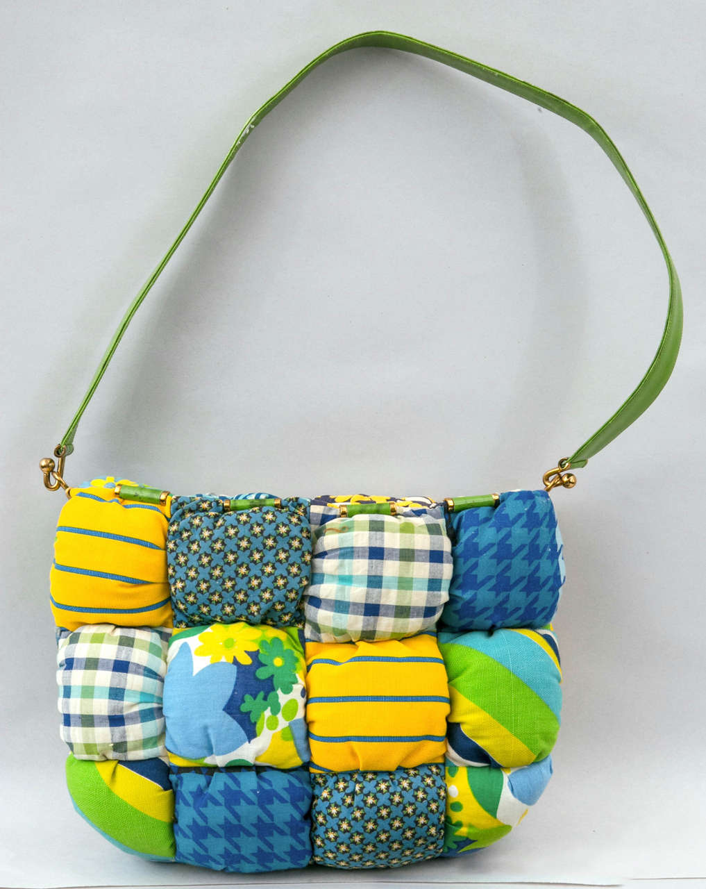 Presented by Funky Finders, limited Judith Leiber textile shoulder bag featuring distinctive flower power prints on a statement quilted surround. Green leather cylinder accents frame the top of purse and compliment the matching color leather strap.