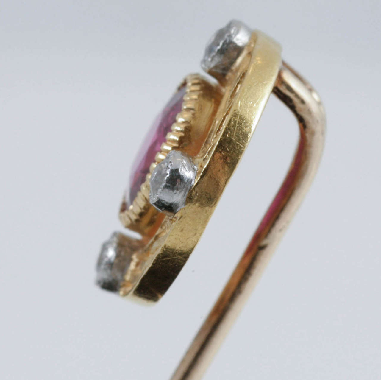 A yellow gold mounted tie pin set with a Burma ruby centre, surrounded by four, old cut brilliant cut diamonds set in platinum within a carved yellow gold setting.
Measures 11mm across.
Antique piece (over 100 years old) in the Edwardian