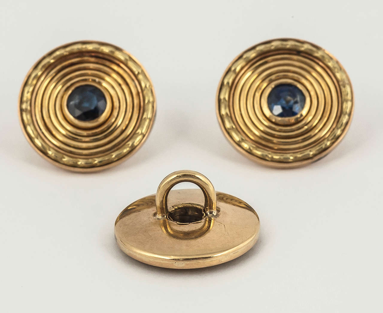 A heavy pair of 18 ct yellow gold cufflinks and three matching buttons with a faceted sapphire centre, bordered in green gold, one side slightly smaller than the other. C 1950