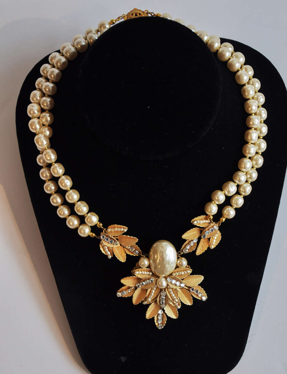 A double-strand pearl necklace with a stylized floral pendant by Miriam Haskell.
Beautiful detailing combining textured gilt metal, faux seed pearls and rhinestones as is typical of Haskell's best work.  Marked on clasp.

Length of center