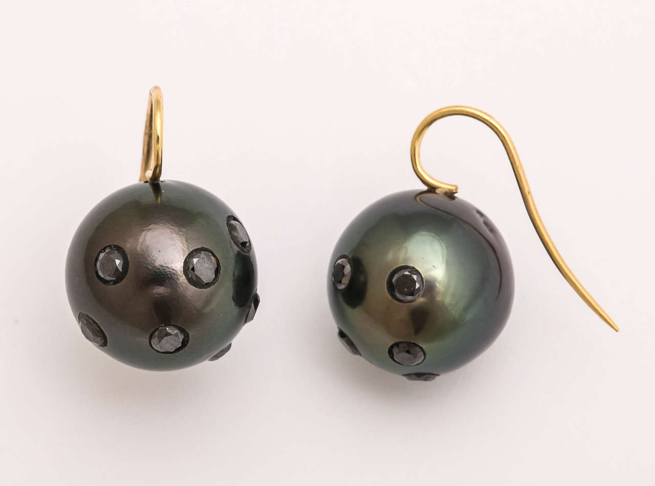 Huge Tahitian black pearls (17 mm) are imbedded with 14  faceted black diamonds. The diamonds are .15 cts each, totaling 2.1 cts. When the light is reflected from the black diamonds, the flash is magical. The pearls hand from an 18 kt  ear wire and