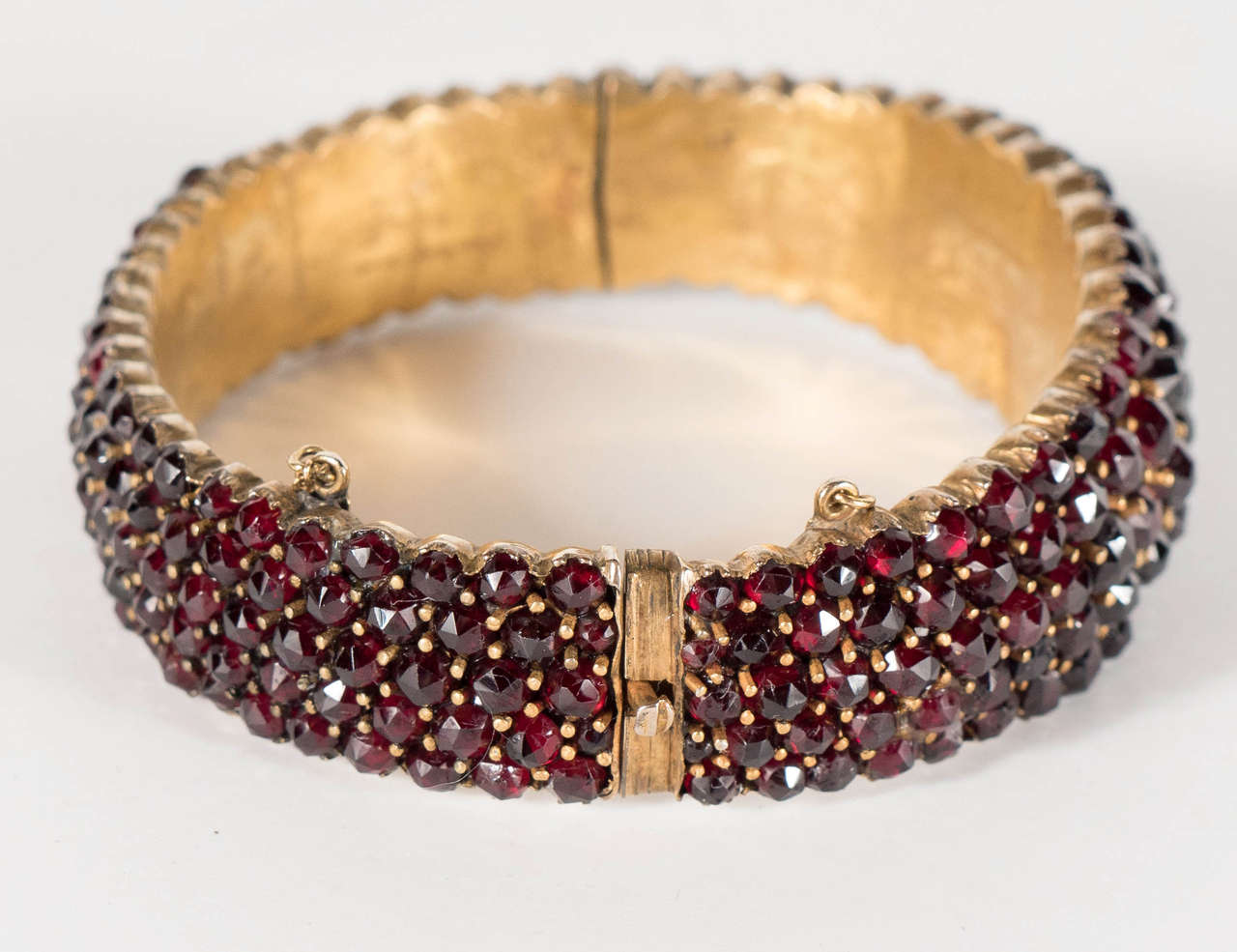 This stunning bracelet features 5 tiers of graduated garnets set in what is called garnet gold which is a sterling silver base washed is gold. It has a hinged bangle design that locks with a safety chain as well.