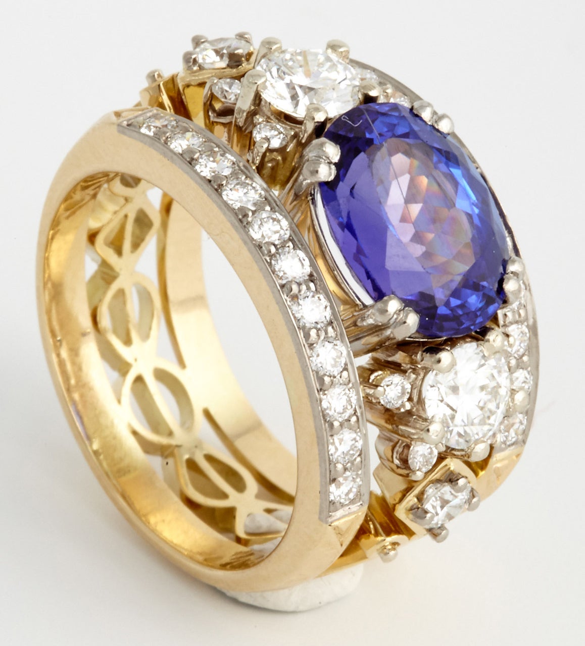 A yellow golden tanzanite and diamond harp ring. Centrally set is an oval mixed cut tanzanite, weight 3.43 ct with a deep blue, triple AAA grade colour. On either side of the tanzanite are two brilliant cut diamonds and above and below are two rows