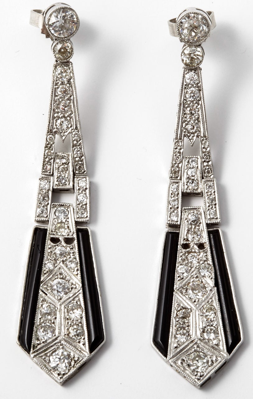 A pair of Art Déco onyx and diamond pendant earrings, set with intermediate brilliant cut and Swiss cut diamonds. Either side of the earrings terminate with in with long narrow tapered cut onyx stones. Total diamond weight is estimated at