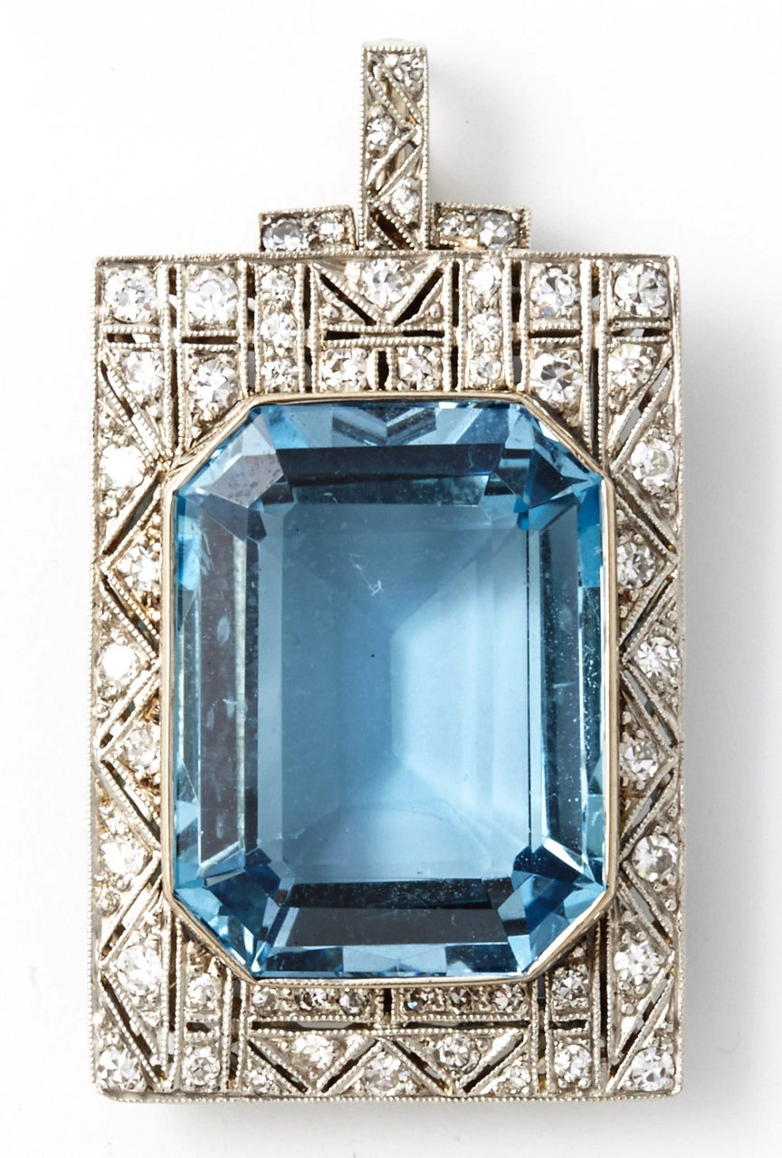An Art Déco pendant/brooche centering an extremely fine example of a modified emerald cut aquamarine with a deep blue colour and a very clean clarity. Dimensions 4.0 x 2.2 cms. Weight circa 19.00 carats total. The aquamarine is surrounded by in an