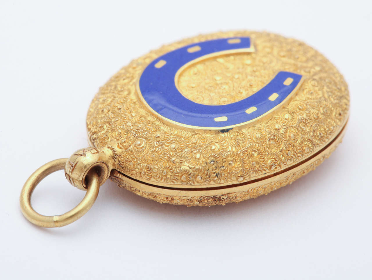 A treat of a locket with outstanding personality and punch, all packed into an inch of length. The textured gold is glistening with engraving that sparkles with  any available light. The reverse is covered with the same sparkle. Whereas the front