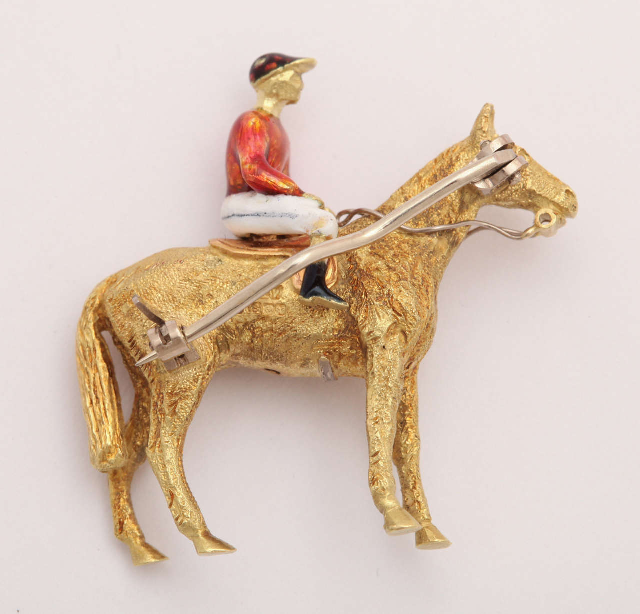 From Great Britain and one of the finest enamel workers in London comes a textured 18 kt and enamel horse and jockey pin. It is a remarkably crafted small sculpture that is three dimensional and stands on all fours. The form of the animal and the