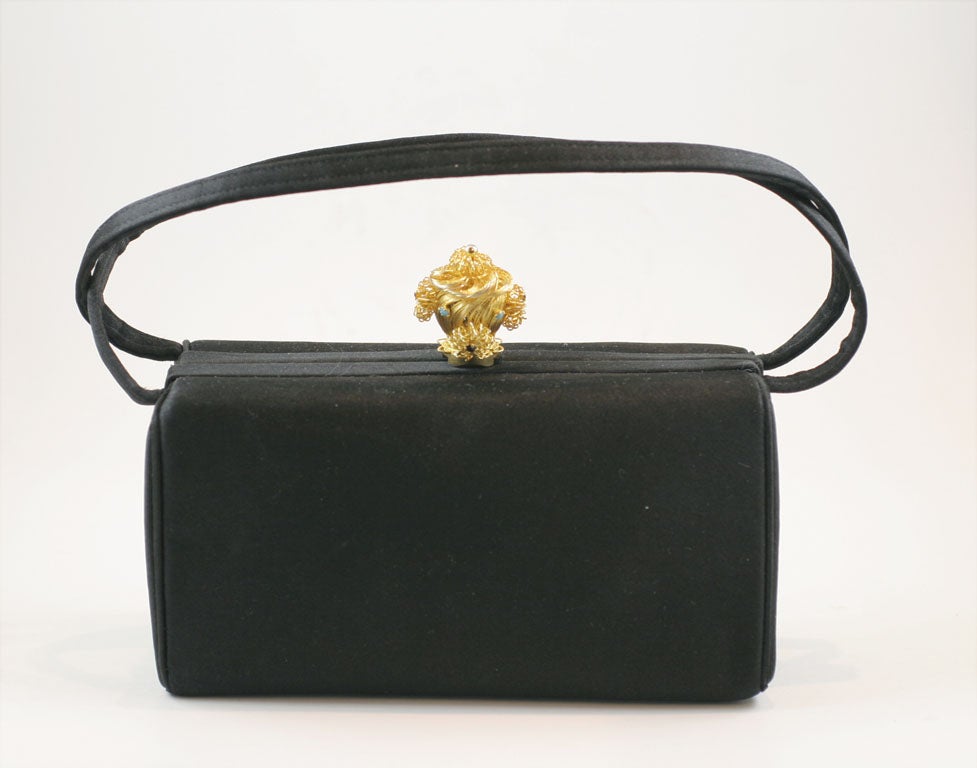 Black satin evening bag from the 1960's with a wire work gold tone poodle clasp. The charming poodle has turquoise stones for the eyes and a jet black rhinestone for the nose. Clasp closes securely with a loud click. Interior is ivory satin and